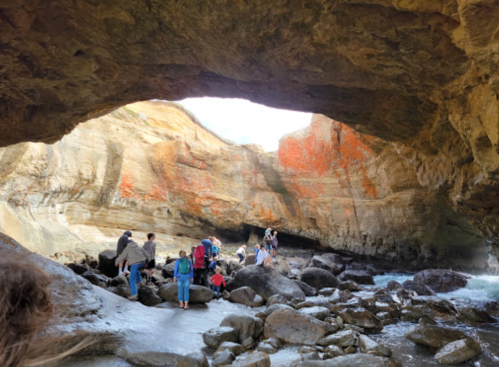 A group of people exploring a rocky cave with colorful walls and a bright opening in the background.