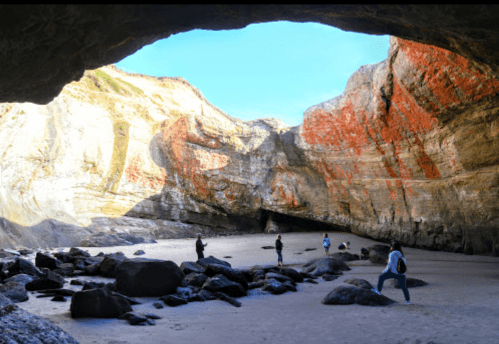 A group of people exploring a large cave with colorful rock formations and a sandy floor.