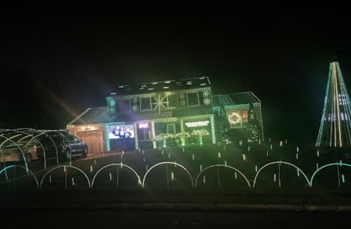 A house decorated with colorful lights for the holidays, featuring a lighted tree and festive displays in the yard.