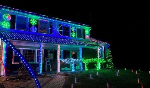 A house decorated with colorful Christmas lights in green, blue, and white, creating a festive nighttime display.