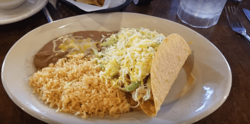 A plate with rice, refried beans, and a taco filled with lettuce and cheese.