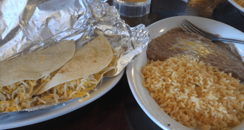 Two soft tacos with cheese, a side of refried beans, and a serving of yellow rice on a plate.