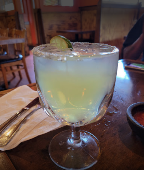 A refreshing margarita in a large glass, garnished with a lime slice and a salted rim, on a wooden table.