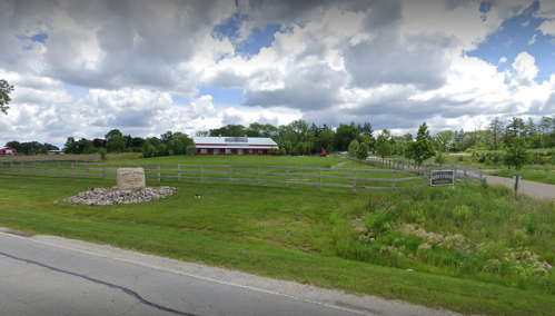 A grassy area with a stone sign, a red barn in the background, and a cloudy sky overhead.