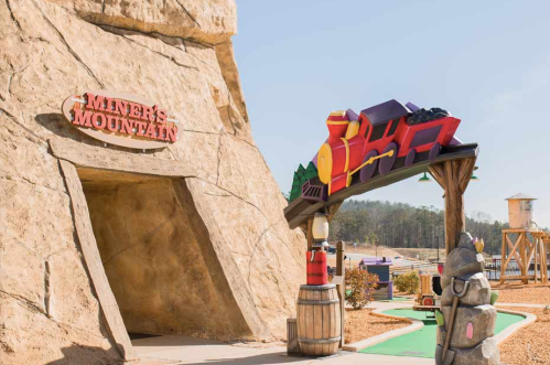 Entrance to Miner's Mountain featuring a colorful train sign and a stone structure in a playful outdoor setting.