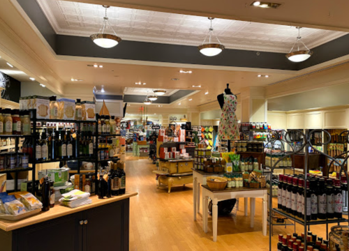 A well-lit store interior filled with shelves of various food products, oils, and a dress on display.