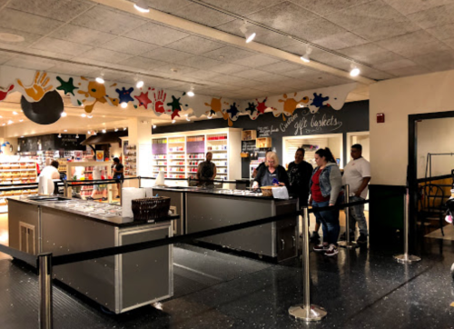 A brightly lit store interior with a checkout area and customers waiting in line. Colorful decorations adorn the walls.