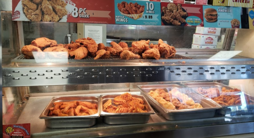 A display case filled with various fried chicken pieces and wings, with trays of additional fried items in front.