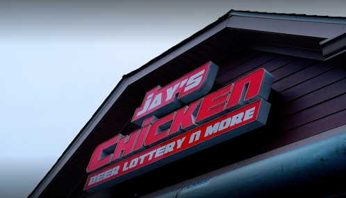 Sign for Jay's Chicken featuring "Beer, Lottery & More" against a cloudy sky.