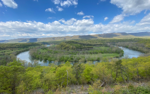 A scenic view of a winding river surrounded by lush greenery and rolling hills under a partly cloudy sky.