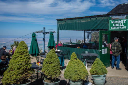 Outdoor dining area of the Summit Grill Restaurant with green umbrellas and scenic mountain views in the background.
