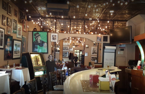 A cozy restaurant interior with a bar, vintage decor, framed photos, and warm lighting.
