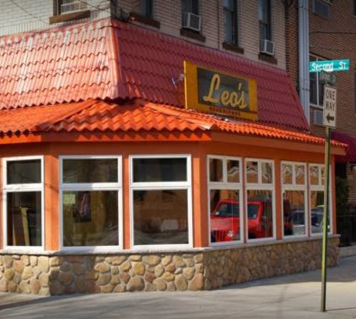 A corner restaurant with a red tiled roof and large windows, featuring a sign that reads "Leo's" on a city street.