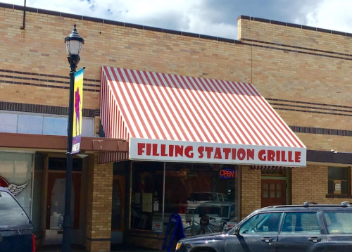 Exterior of Filling Station Grille with a red and white striped awning and an "Open" sign in the window.