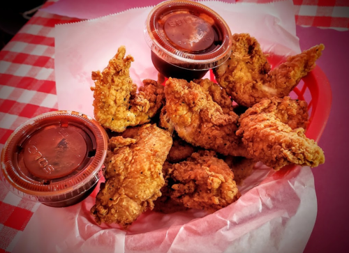 A basket of crispy fried chicken wings with two dipping sauces on a checkered tablecloth.