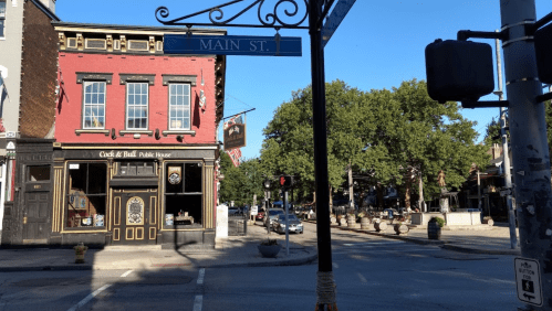 A street view of a red brick building with a sign for Main St, featuring a pub and trees lining the road.