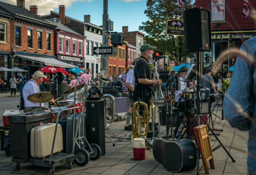 A lively street scene with musicians playing instruments, including drums and brass, in a colorful town square.