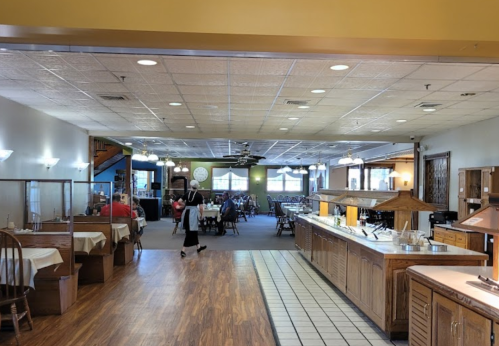 A spacious restaurant interior with dining tables, a buffet area, and patrons enjoying their meals.