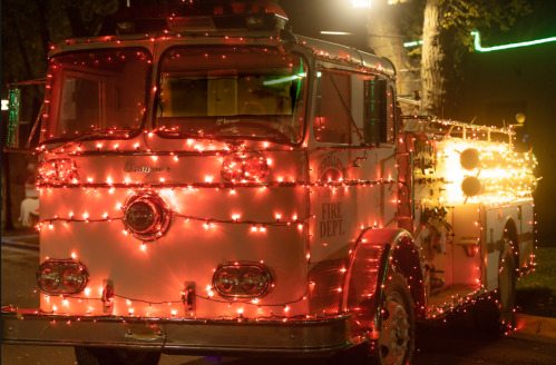 A vintage fire truck adorned with bright red and white lights, parked at night with festive decorations.