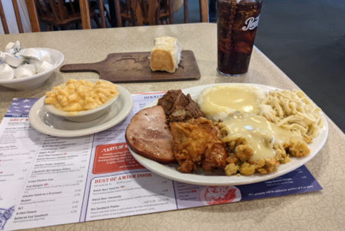 A plate of comfort food featuring fried chicken, ham, mashed potatoes, stuffing, and macaroni and cheese, with a drink.