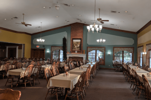 A spacious dining room with wooden chairs and tables, featuring a fireplace and large windows.