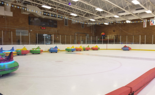 Colorful bumper cars on an ice rink, with festive lights and decorations in a spacious indoor arena.