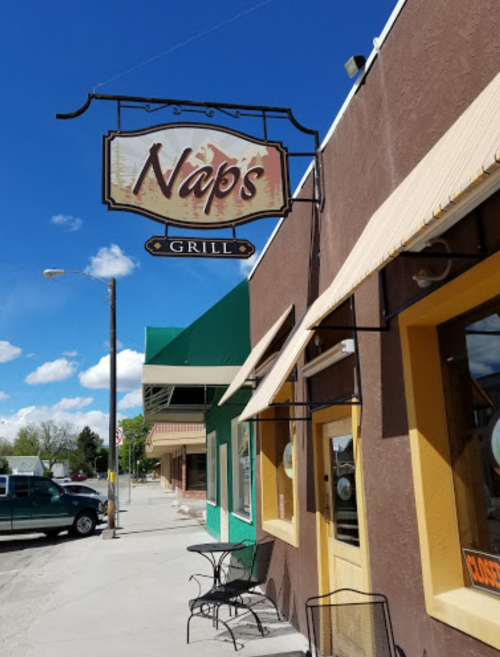 Sign for "Nap's Grill" on a building with outdoor seating, under a blue sky with scattered clouds.