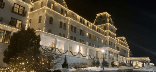 A beautifully lit historic hotel at night, adorned with festive lights and surrounded by snow.