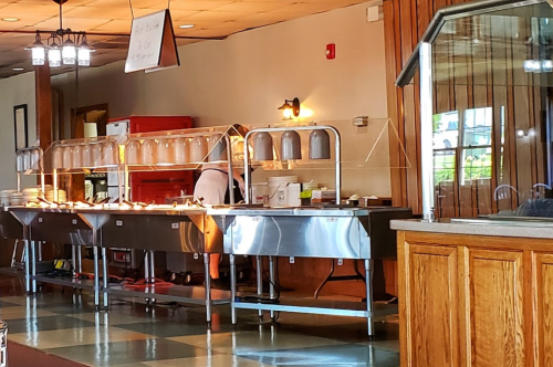 A buffet setup with metal trays and a person serving food in a spacious dining area.
