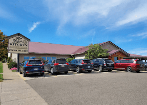 A restaurant with a maroon roof and several parked cars in front, set against a clear blue sky.