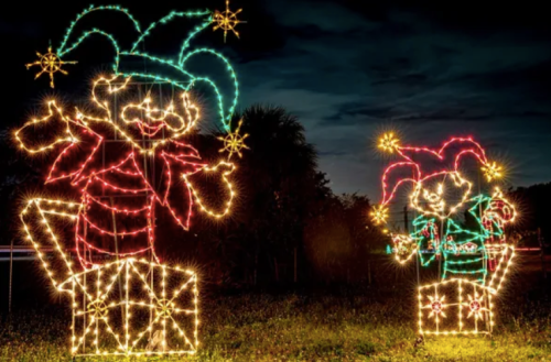 Two colorful jester figures made of holiday lights, standing on gift boxes against a dark sky.