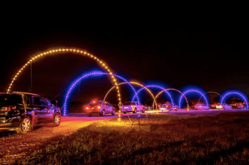 A nighttime scene with cars driving under colorful illuminated arches along a dark road.