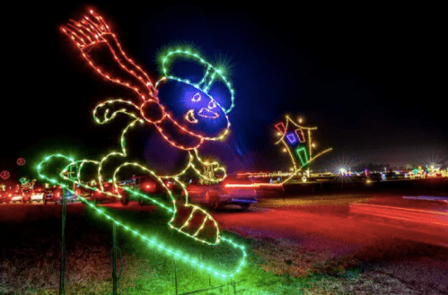 A colorful light display features a snowman on a snowboard, with a house illuminated in the background at night.