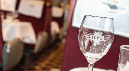 A close-up of a glass with "Cuyahoga" logo, set on a dining table in a train car with elegant decor.