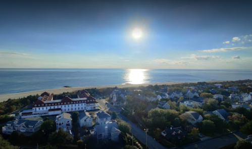 A serene coastal view with a shining sun reflecting on the water, overlooking a beach and nearby houses.