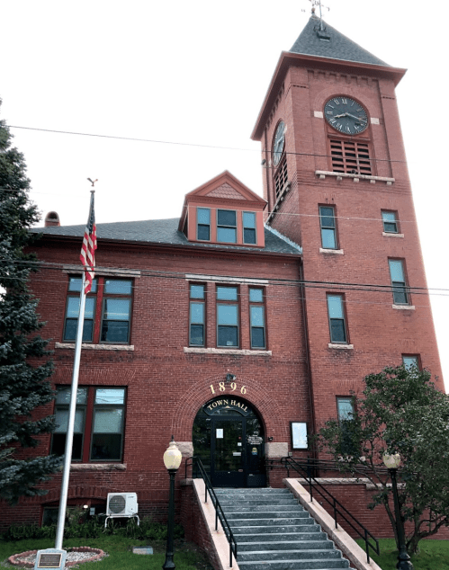 Historic red brick town hall building with a clock tower, established in 1896, featuring an American flag out front.