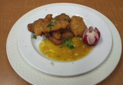 A plate of golden-brown fried pieces with a tangy sauce and a decorative radish on the side.