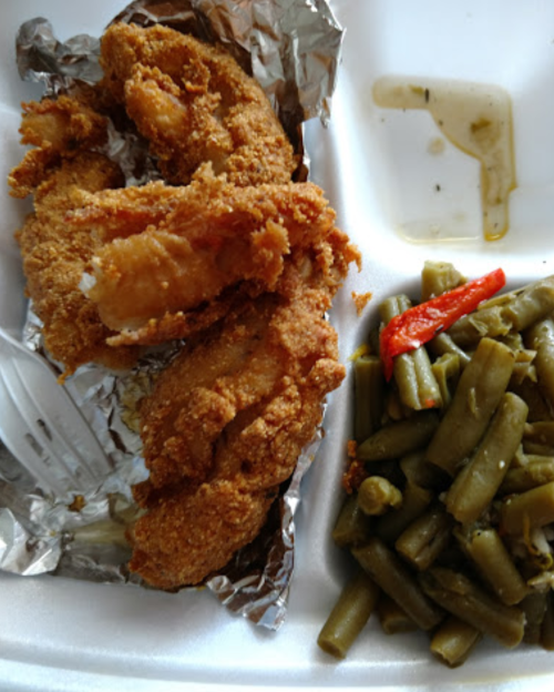 A plate with fried chicken pieces wrapped in foil and a side of green beans with a red pepper.