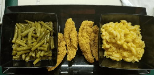 A black plate with three sections: green beans, fried fish fillets, and macaroni and cheese.