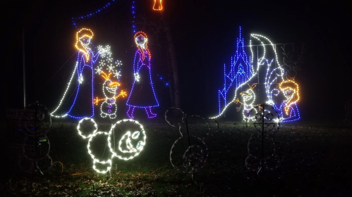Colorful holiday lights depict characters from a winter scene, including snowmen and a castle, against a dark background.