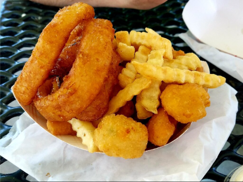 A bowl of crispy onion rings and golden crinkle-cut fries, served with small fried snacks.