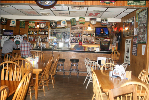 A cozy bar interior with wooden tables, a long counter, and patrons enjoying drinks in a warm, inviting atmosphere.