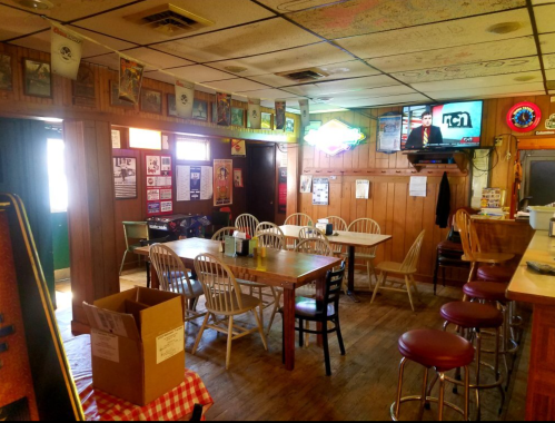 Cozy diner interior with wooden walls, tables, chairs, and a TV showing news, featuring a casual, welcoming atmosphere.