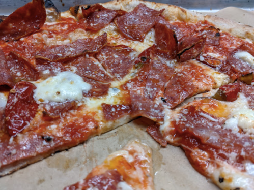 A close-up of a pepperoni pizza with melted cheese and a crispy crust on a brown paper surface.