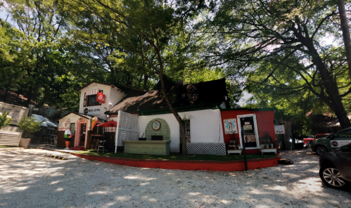A charming building with a thatched roof, surrounded by trees and a gravel path, featuring colorful signage.