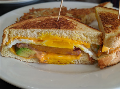 A close-up of a grilled sandwich with layers of egg, cheese, and sausage, served on toasted bread.