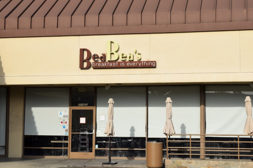 Sign for Bea Bea's restaurant, featuring the tagline "breakfast is everything," with outdoor seating umbrellas.