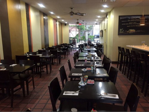 Interior of a restaurant with empty tables, black chairs, and colorful walls, featuring a bar area in the background.