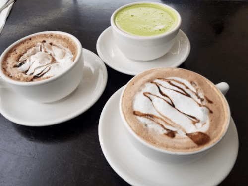 Three cups of beverages on saucers: two with chocolate and whipped cream, one with green tea foam.