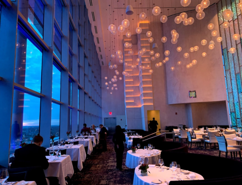 Elegant restaurant interior with large windows, soft lighting, and tables set for dining, creating a cozy atmosphere.